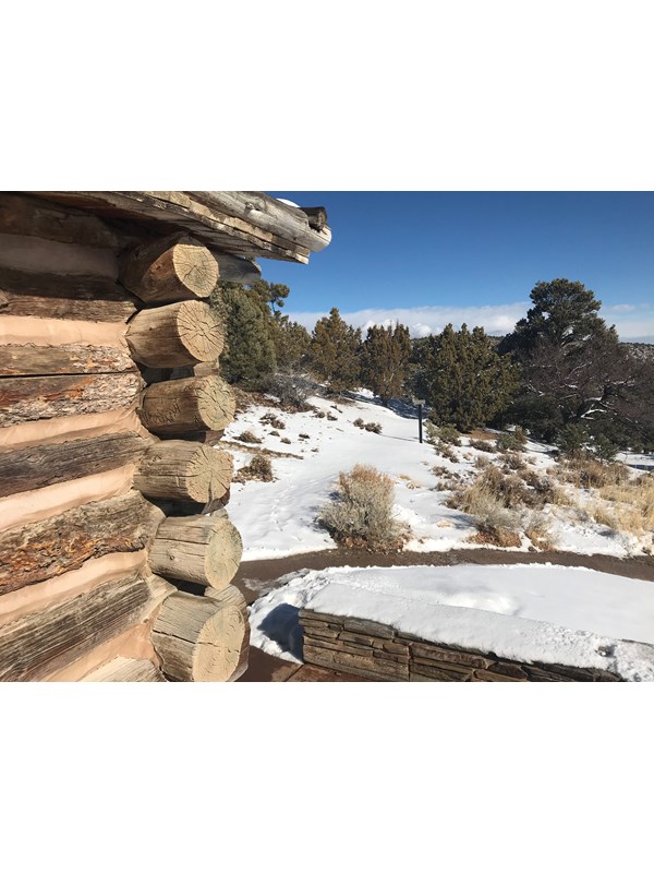 The edge of a log cabin with large beams sits to one side, with a trail stretching forward in snow