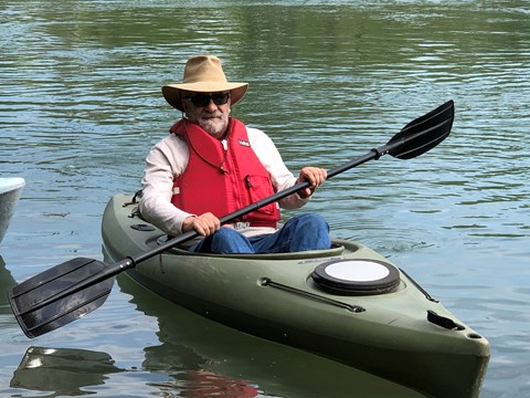 a man wearing hat, sunglasses and red pfd in a green kayak holding a black paddle on the water
