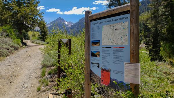 Trailhead sign next to trail with mountains in the distance