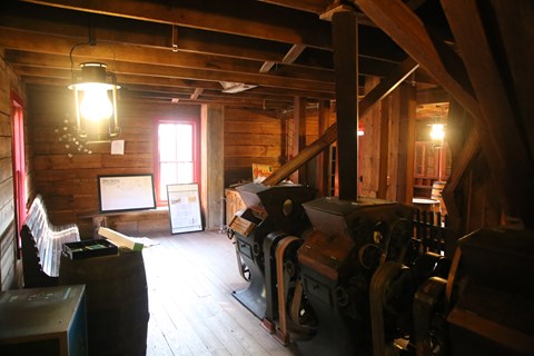 Wooden and iron machines sit on a wood floor with cutes leading to them.