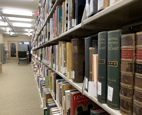 Library shelves in a basement room stacked with books across the shelves.