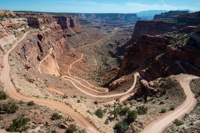 A light beige unpaved road winding down a steep, multicolored sandstone canyon