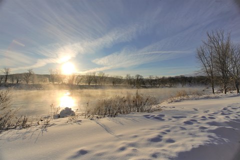 A snow-covered trail looking out at the sun shining on the Delaware River.
