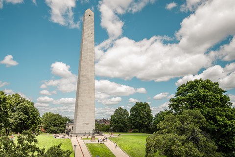 The tall obelisk monument stands under a bright blue sky in the middle of curated grassy grounds