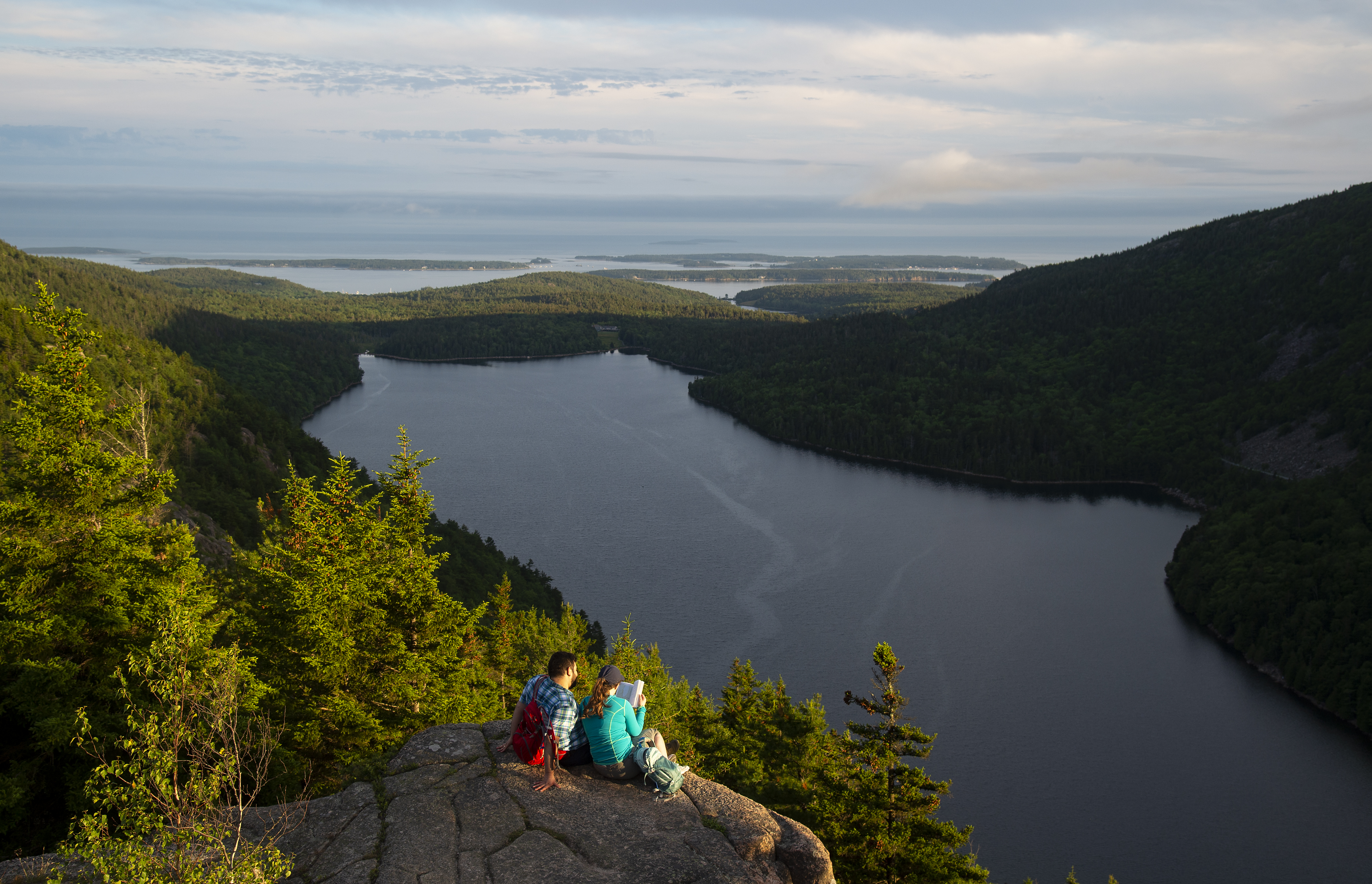 Visitors sitting on a rock ledge overlooking a lake