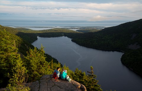 Visitors sitting on a rock ledge overlooking a lake