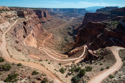 A light beige unpaved road winds back and forth down colorful sandstone walls.