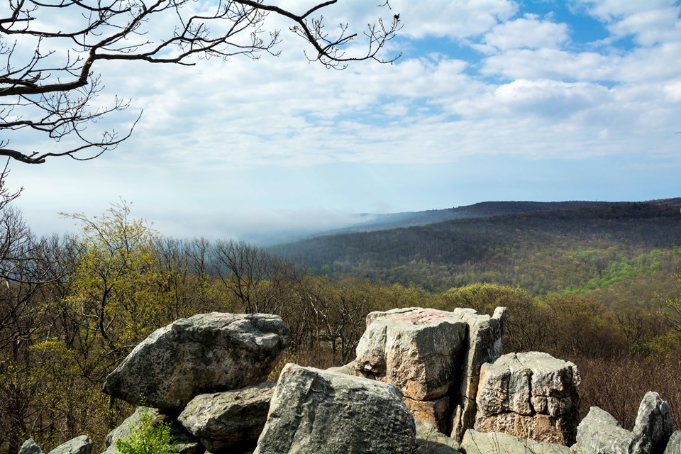A jumble of large boulders is visible with a sweeping mountain view behind it.
