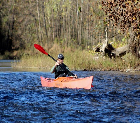 A man in a red canoe floating down a turbelant river with fall colors in background