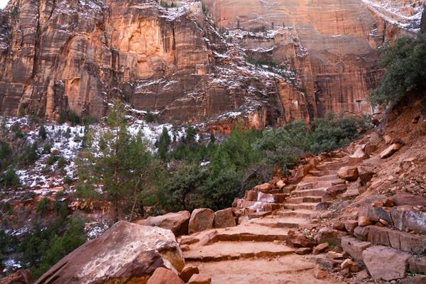 A set of red sandstone stairs lined with loose rocks and green foliage leads out of frame.