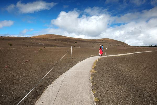 A man and woman walking on a paved path through a barren landscape covered by cinders