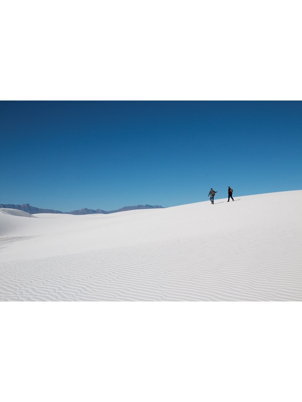 Two people silhouetted on top of a white dune with blue sky overhead