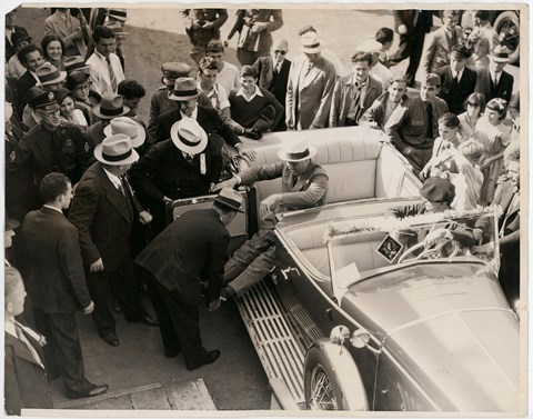 An eager crowd watches as Secret Service agents straighten and lock FDR’s leg braces in preparation