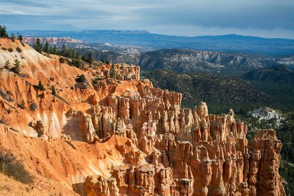 Vibrant red rock cliffs stand above forests with a distant plateau along the horizon