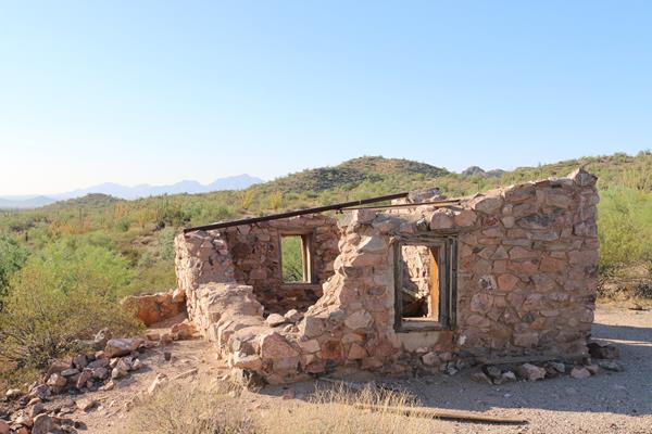 Historic one-room building made with stone walls and no roof, located in a desert.