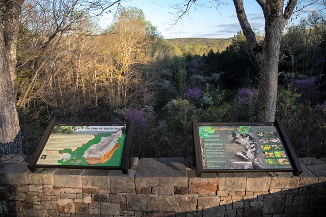 Two information panels on a low stone wall overlooking a forested valley in autumn