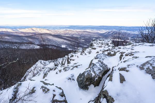 Snow covered rocks lie in the foreground of a view into a blue valley below.