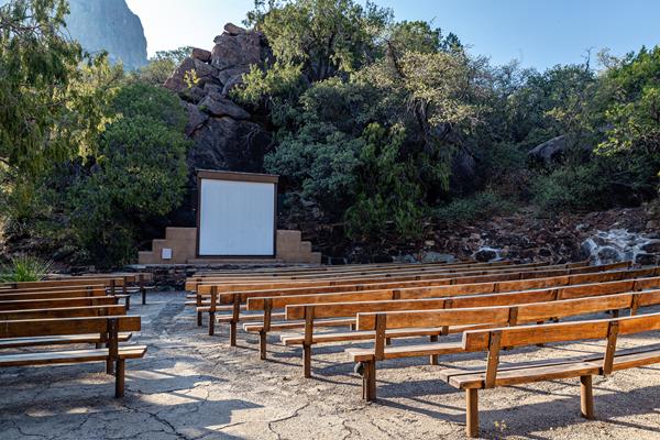 An outdoor screen and small stone stage are surrounded by wooden benches