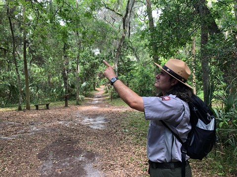 a ranger with a backpack in the woods pointing