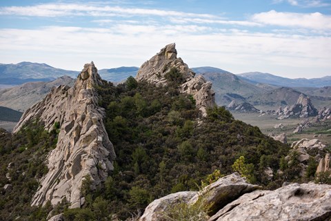 2 prominent granite features jut up in the foreground with a rocky mountainous landscape behind.