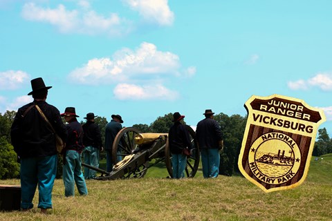Several men dressed in civil war era uniforms stand near a cannon. An image of a wooden badge