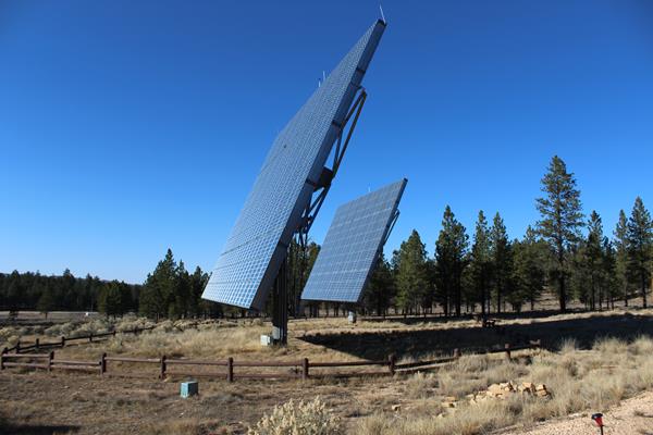 Two solar panels stand in field surrounded by brown wooden fence