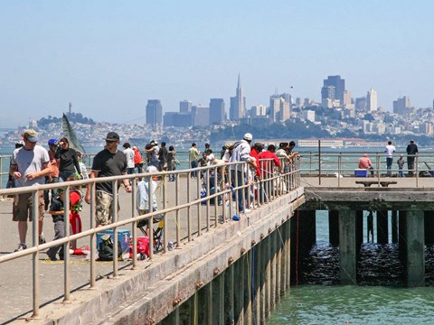 Looking down the length of a fishing pier, scattered with people walking and fishing.