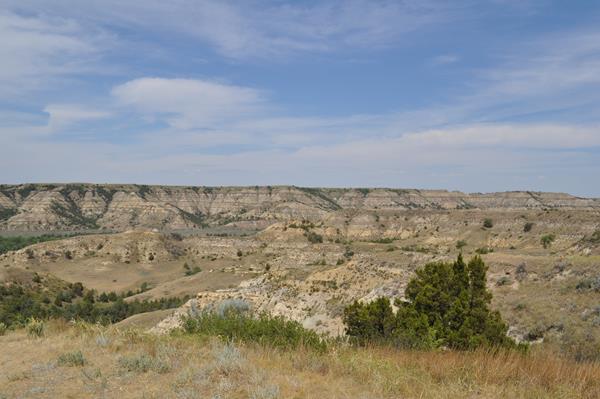 A view across a valley in Theodore Roosevelt National Park, under a blue sky.