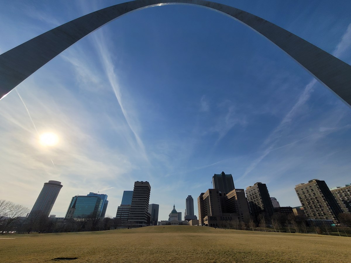the arch curving overhead against a blue sky, city buildings behind
