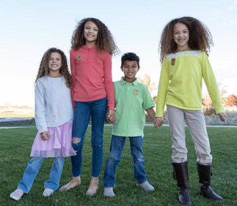 Four kids in bright colored clothes stand in a grassy field.