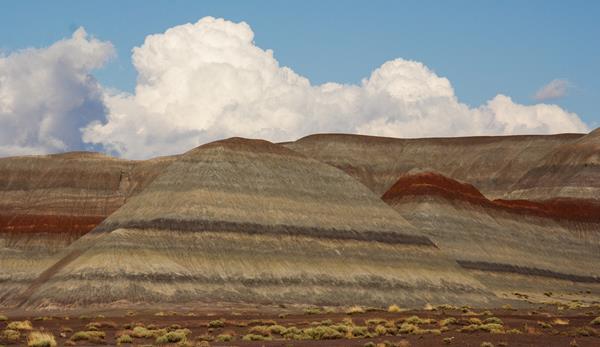 Colorfully banded badlands against a puffy white cloud and blue sky.