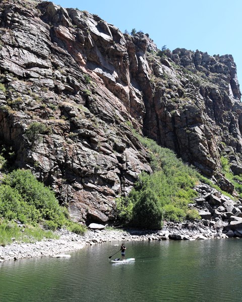 A person standup paddleboarding on a reservoir between steep cliff walls