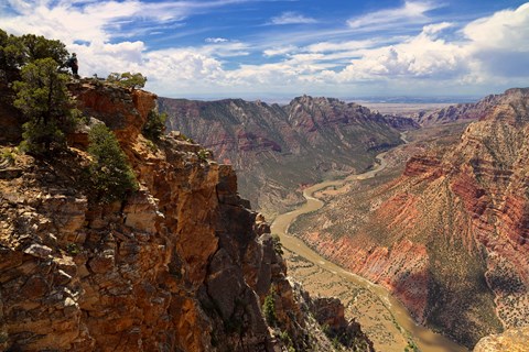 Large walls of orange red rock rise as a river flows through a deep canyon.