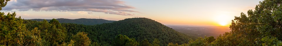 A sunset over a round hill spilling into a valley
