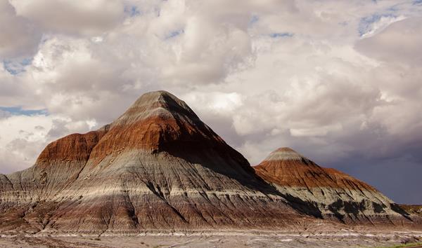 Red and gray badland hills against a mostly cloudy sky.