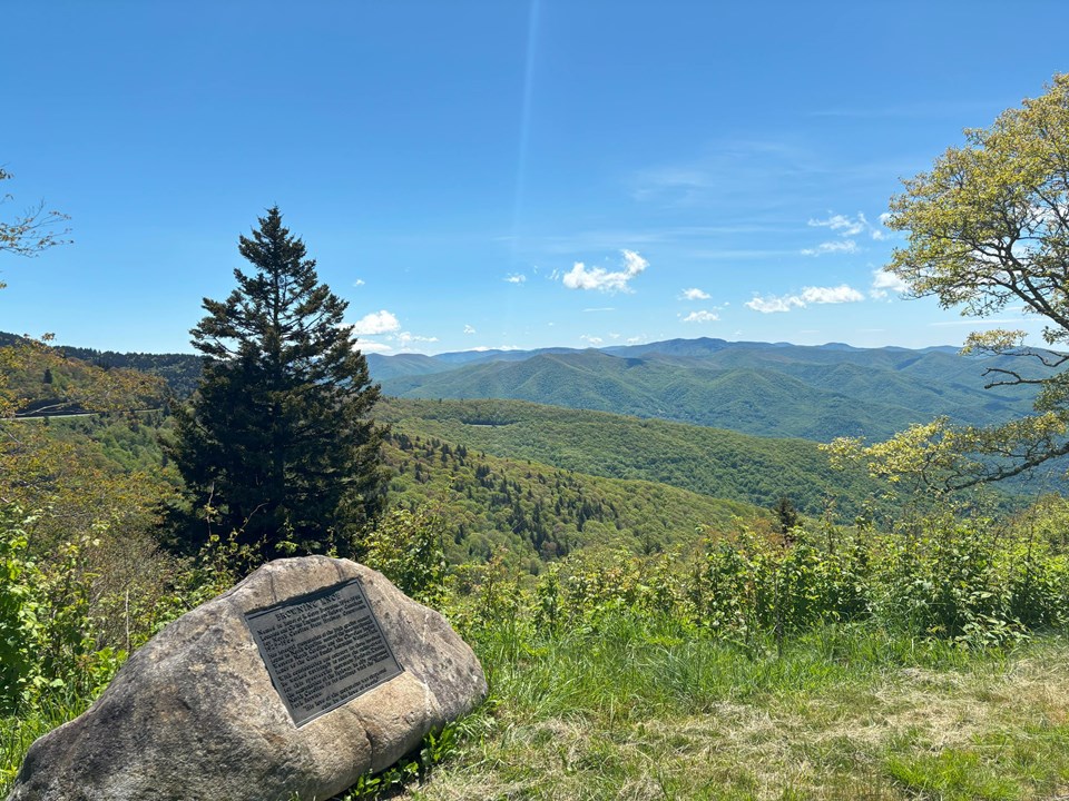 View of scenery with multiple mountain ranges. Historical marker on boulder in foreground