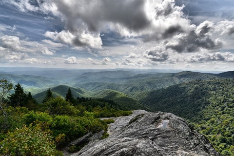 A rocky outcrop looks out over green layered mountains and white clouds