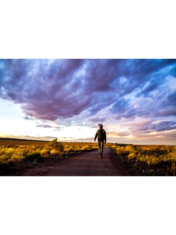 Man walking a trail under a sunset sky with clouds