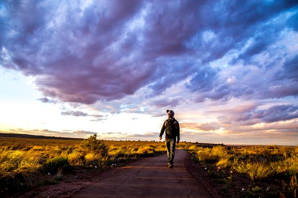 Man walking a trail under a sunset sky with clouds