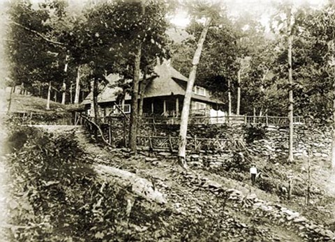 A historic black and white photo from the early 1900s of a rustic lodge in a forest.