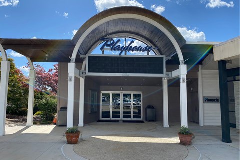 Exterior entrance to a theater with a curved roof that reads “Playhouse”.