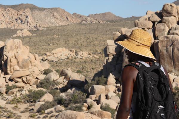 A hiker looking through a rocky landscape to a valley with mountains in the distance.