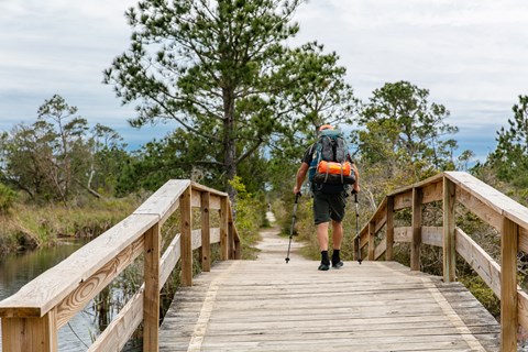 A backpacker crosses over a bridge with poles in hand.