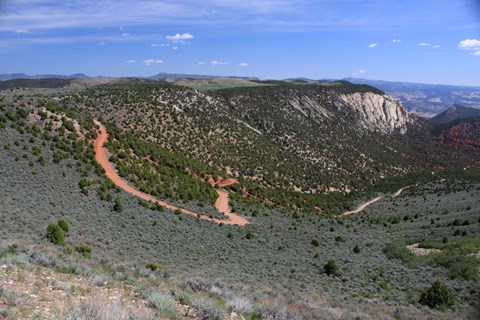 a red colored dirt road winds down a steep slope