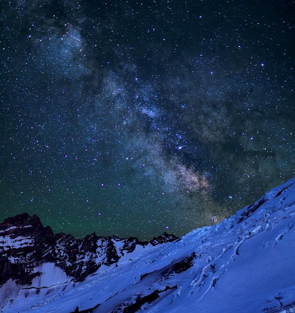 Stars and milky way cover the sky above the glaciated ridges of Mount Rainier.