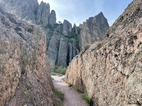 Trail passing through low rock walls with steep rock cliffs towering ahead.