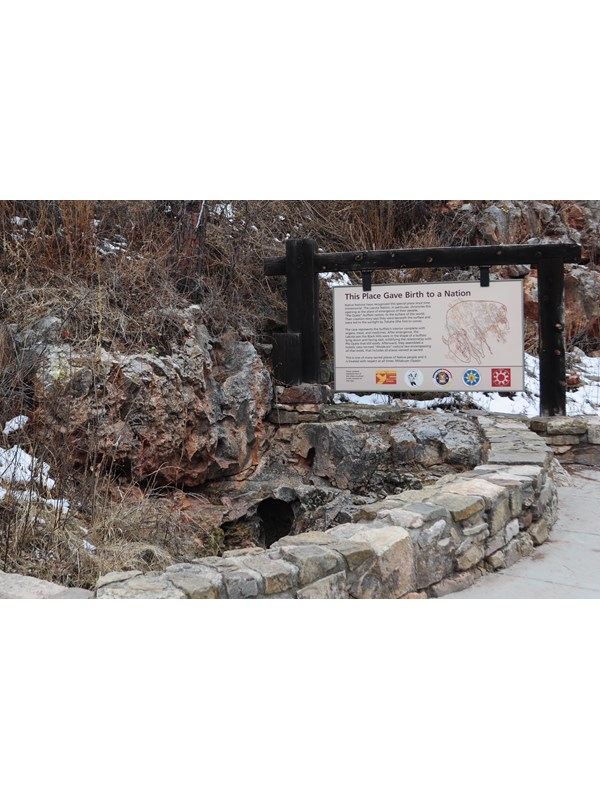 a small hole in a stone depression next to a large sign and short rock wall