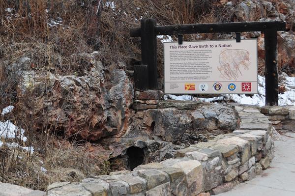 a small hole in a stone depression next to a large sign and short rock wall