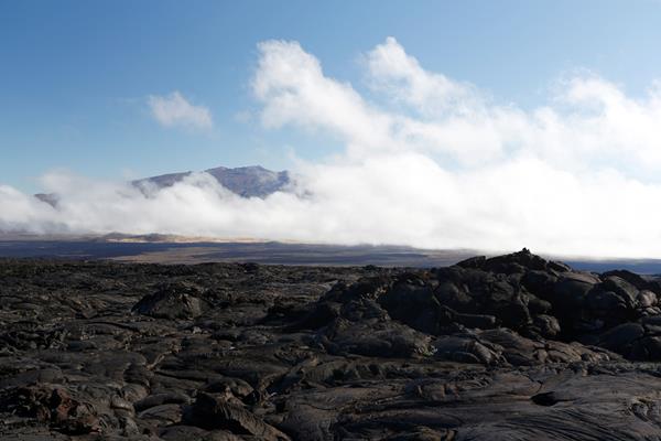 Black lava fields with a distant mountain obscured by clouds.