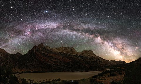 A band of brightly lit stars sweeps across the sky above a mountain.